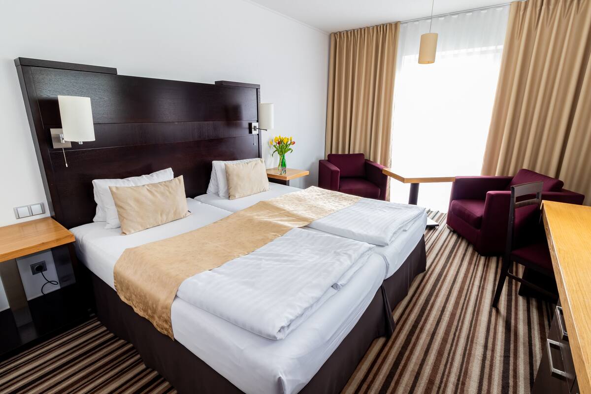 Une chambre d’hôtel avec un grand lit, deux tables de chevet, un bureau, une chaise et une fenêtre avec des rideaux.