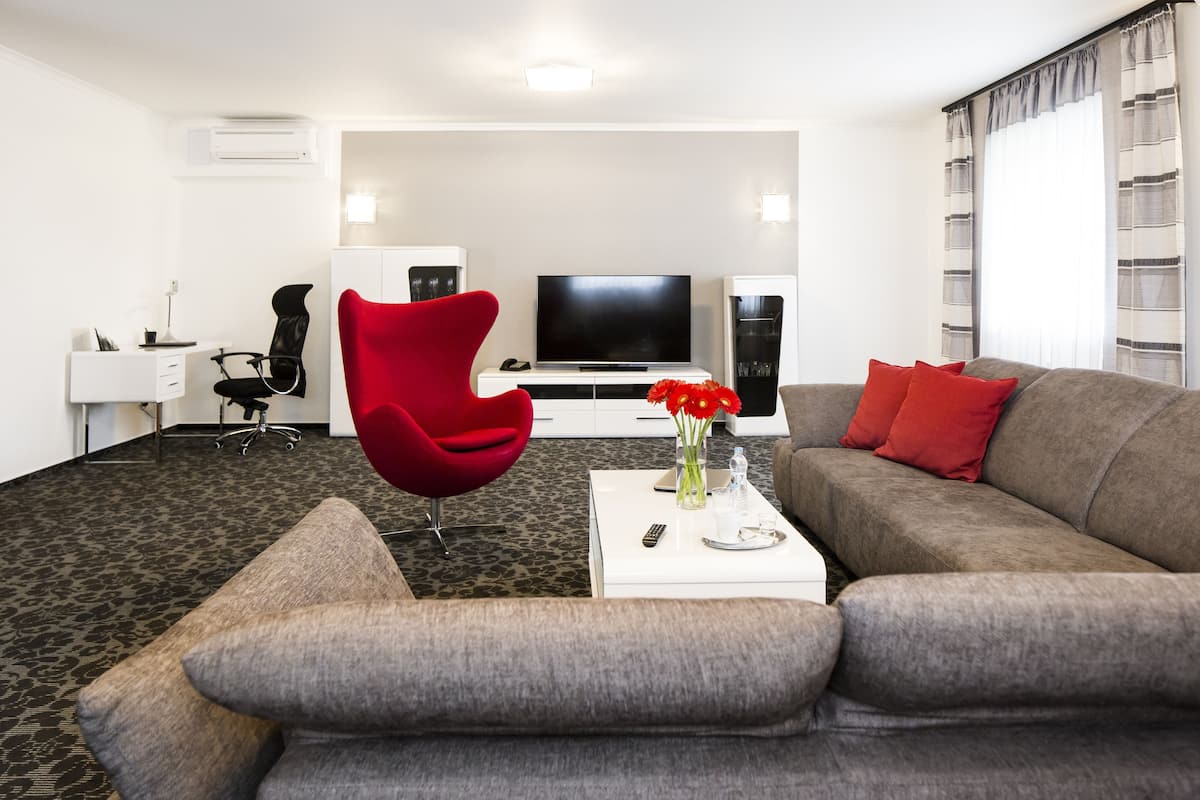 Un salon moderne avec un canapé gris, un fauteuil rouge et un téléviseur à écran plat.