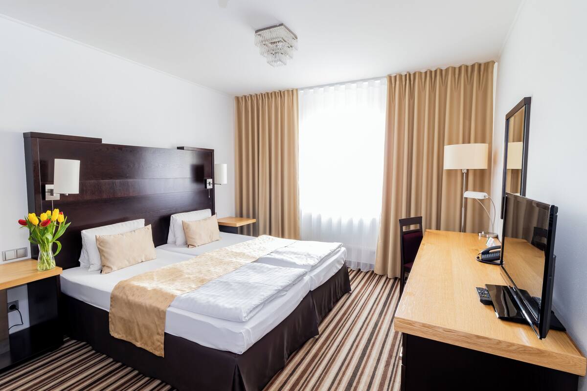 Une chambre d’hôtel avec un grand lit, un bureau avec un ordinateur, une chaise, une lampe et un miroir.