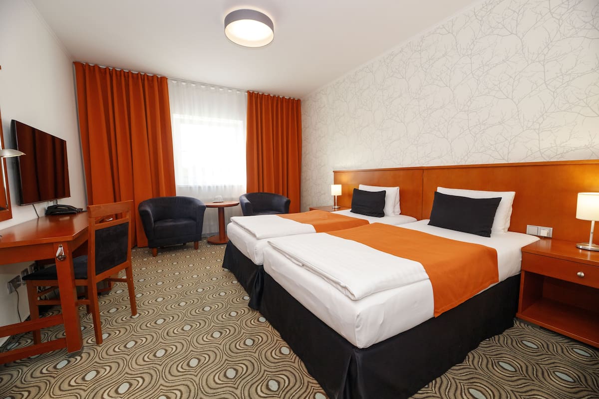 Une chambre d’hôtel avec deux lits, un bureau, une chaise, une télévision et une fenêtre avec des rideaux.