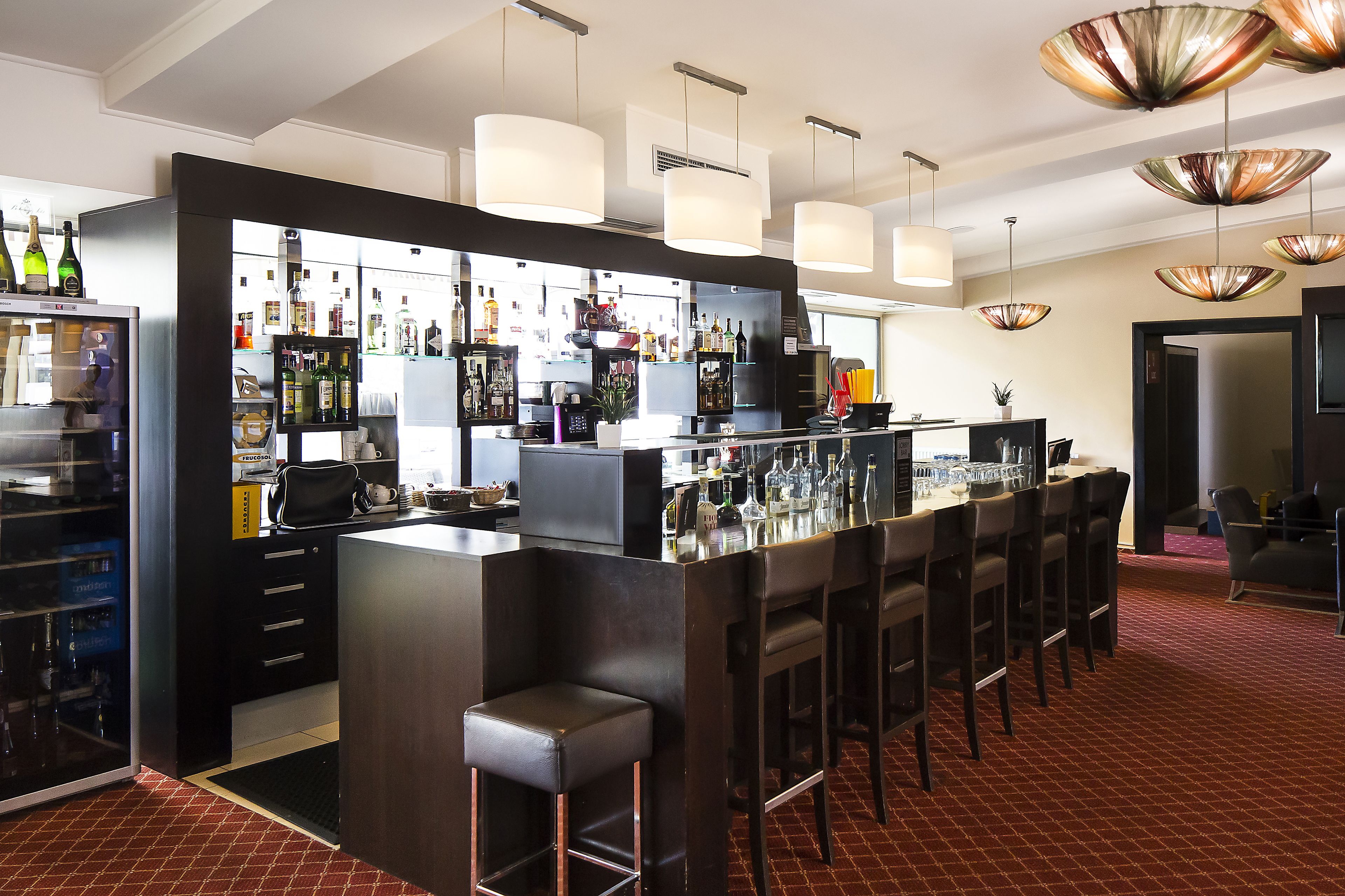Een bar met een toonbank, krukken en diverse flessen en glazen.