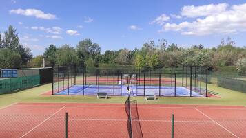 Een tennisbaan met net, omgeven door een hek en groen.