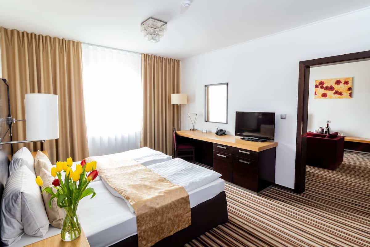 Une chambre d’hôtel avec un lit, un bureau, une télévision et un vase rempli de fleurs.