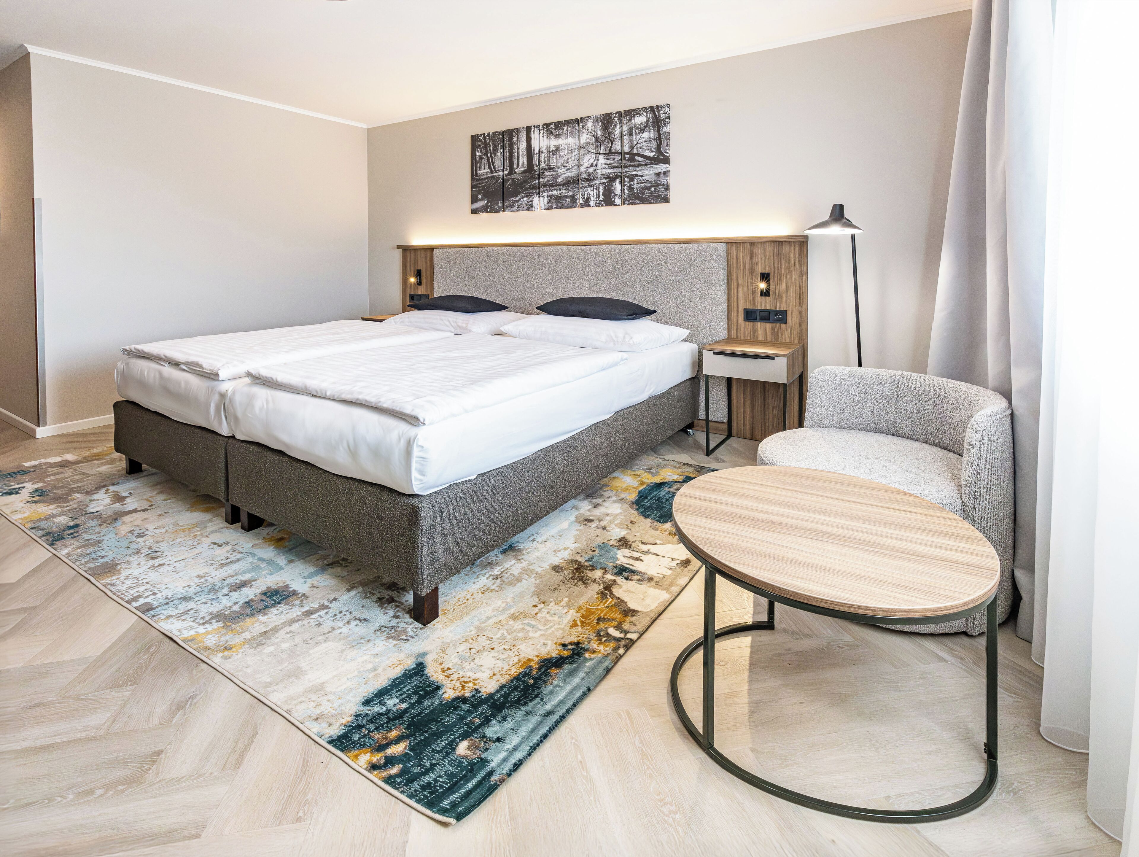 Quarto moderno com uma cama grande, mesas de cabeceira, uma cadeira e um tapete.