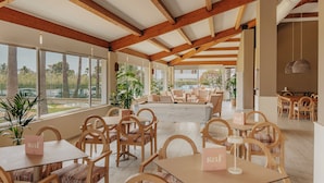 A spacious indoor area with wooden beams, large windows, and multiple seating arrangements.