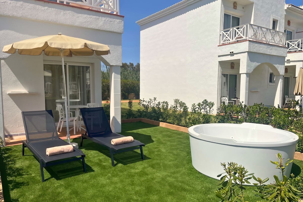 Un espace aménagé au bord de la piscine, avec des chaises longues, un jacuzzi et un jardin.