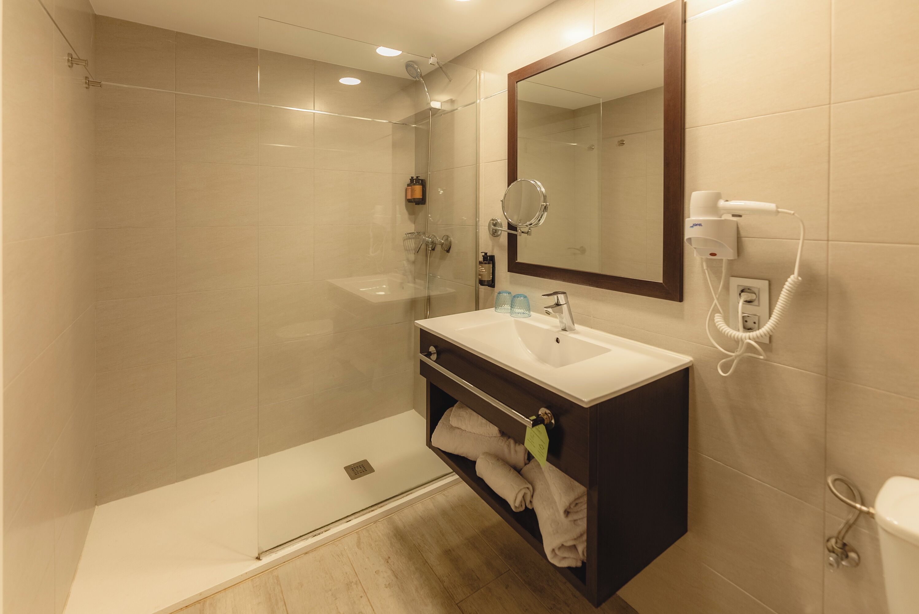 A modern bathroom with a glass shower enclosure, a vanity with a mirror, and a hairdryer on the wall.