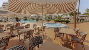 A poolside area with striped umbrellas, wicker furniture, and a hot tub.