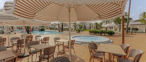 A poolside area with striped umbrellas, wicker furniture, and a hot tub.