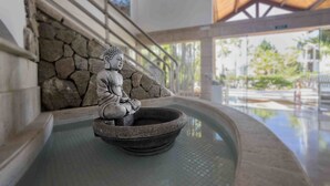 A Buddha statue in a stone basin, a stone wall, and a view of a pool area with a wooden roof structure.