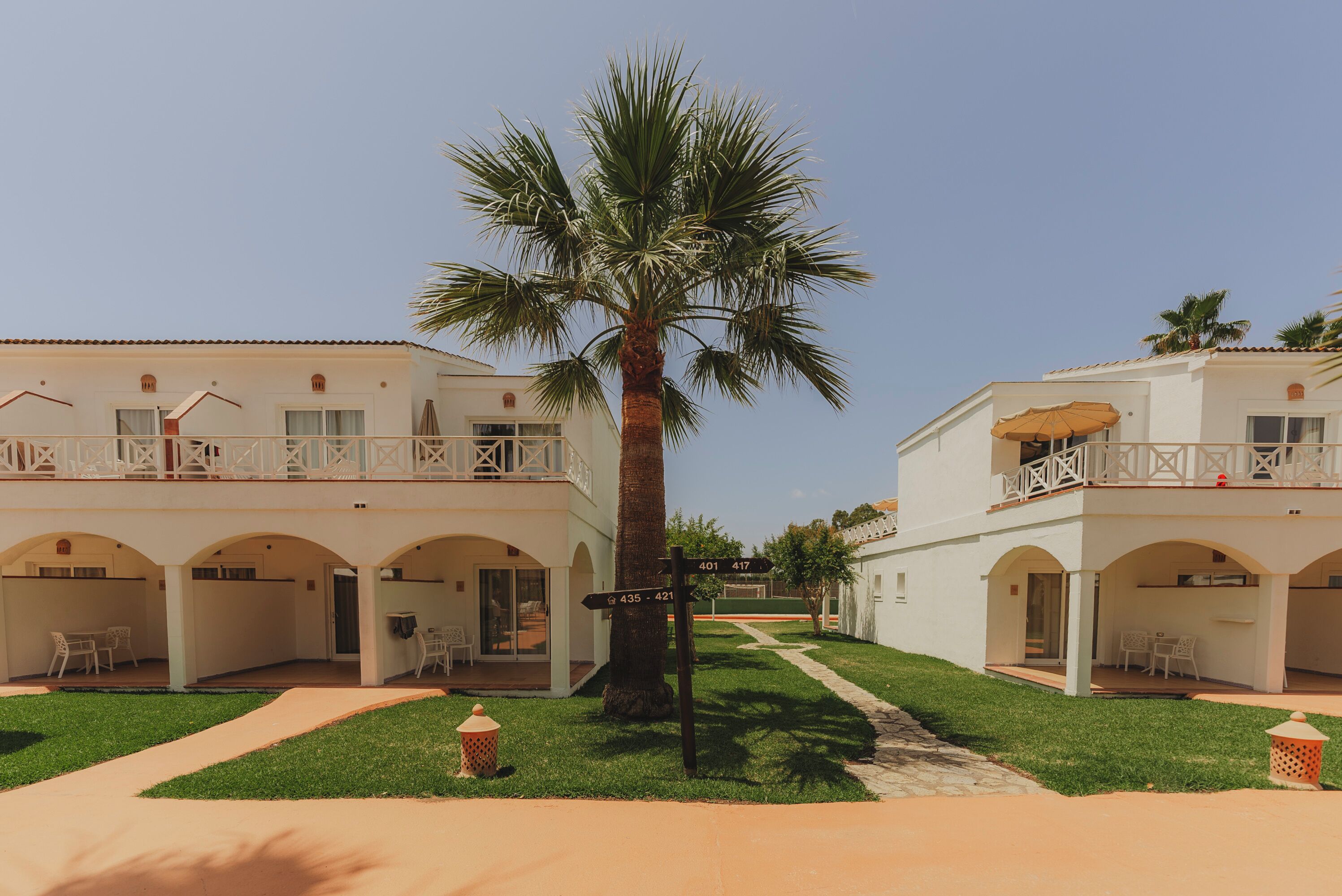 A two-story building with a central palm tree, outdoor seating, and a clear sky.