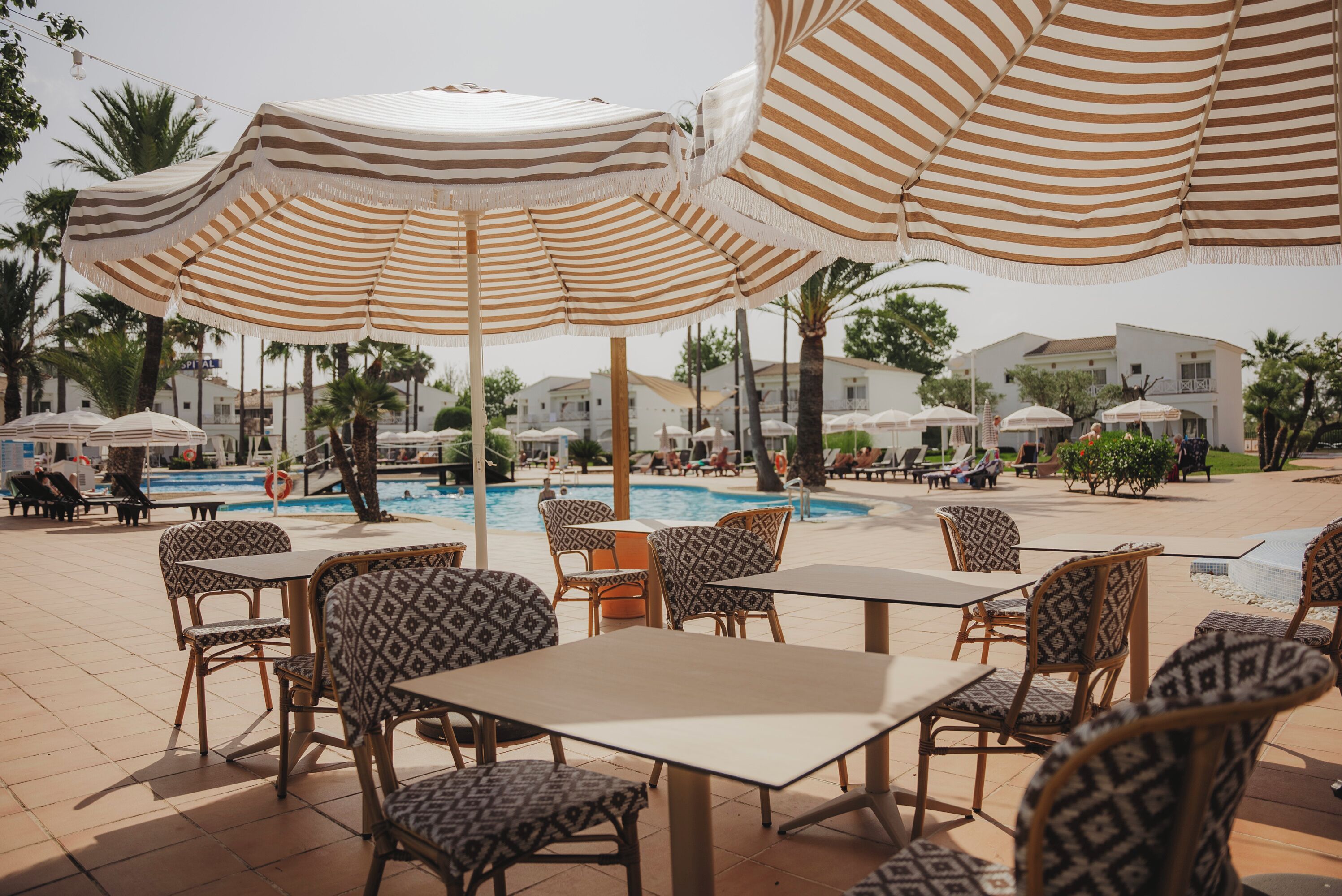 Un espace aménagé au bord de la piscine, avec des parasols à rayures, des chaises et des tables aux motifs variés.