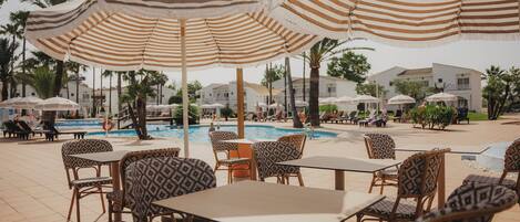 Un espace aménagé au bord de la piscine, avec des parasols à rayures, des chaises et des tables aux motifs variés.