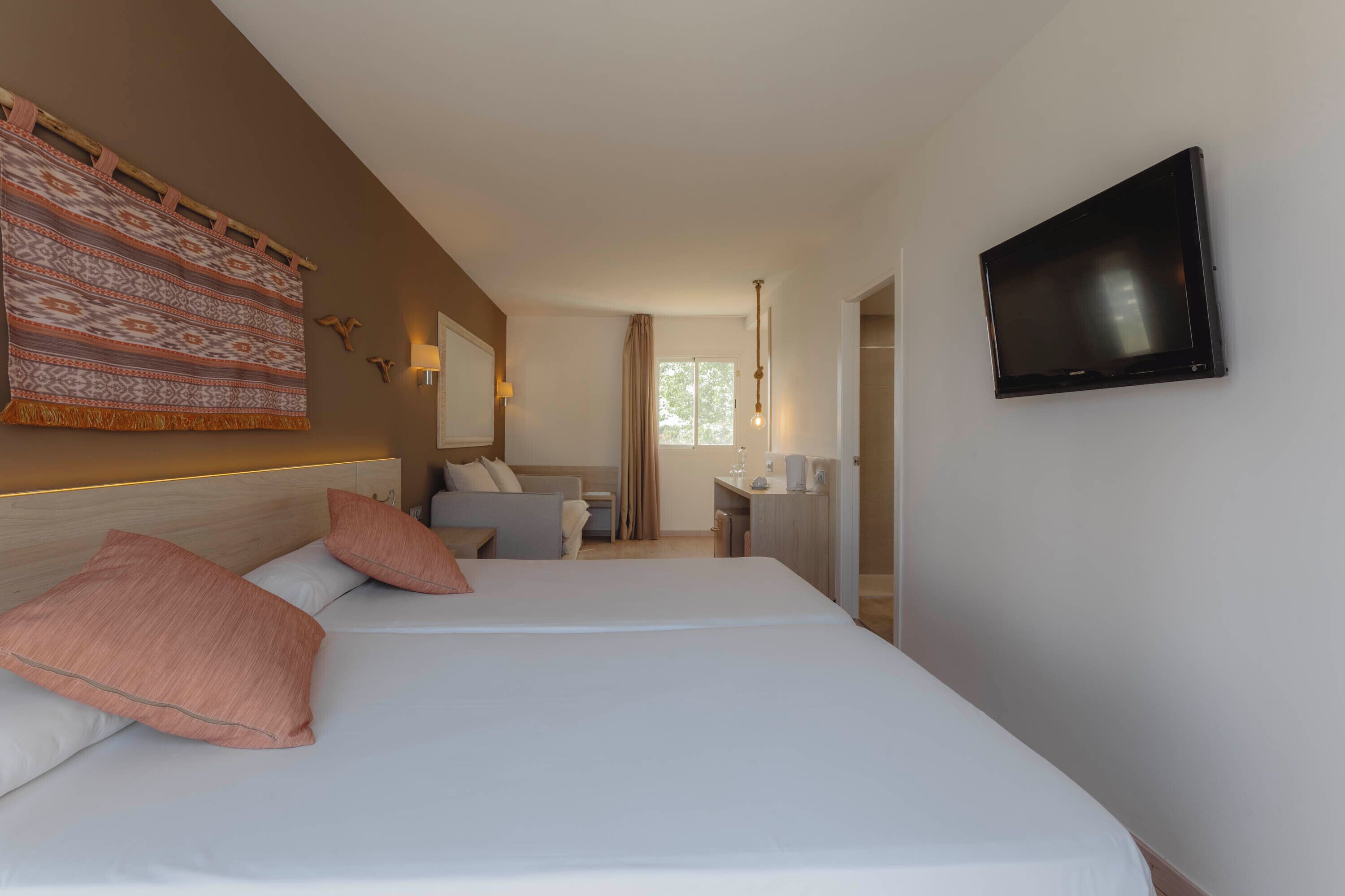 A hotel room with two beds, a TV, a desk, and a window.
