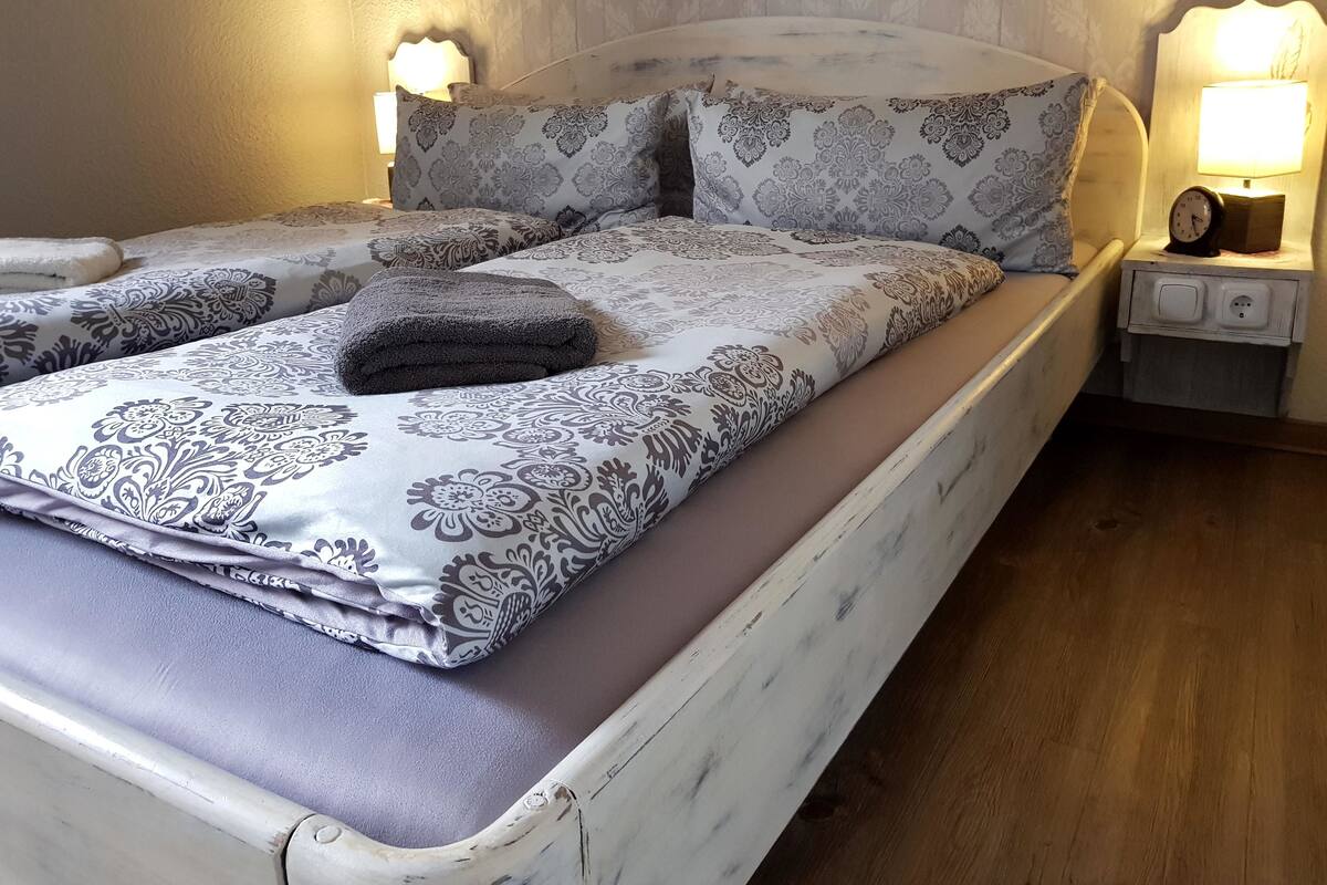 Un lit double avec une literie à motifs, deux tables de chevet avec des lampes et un plancher en bois.