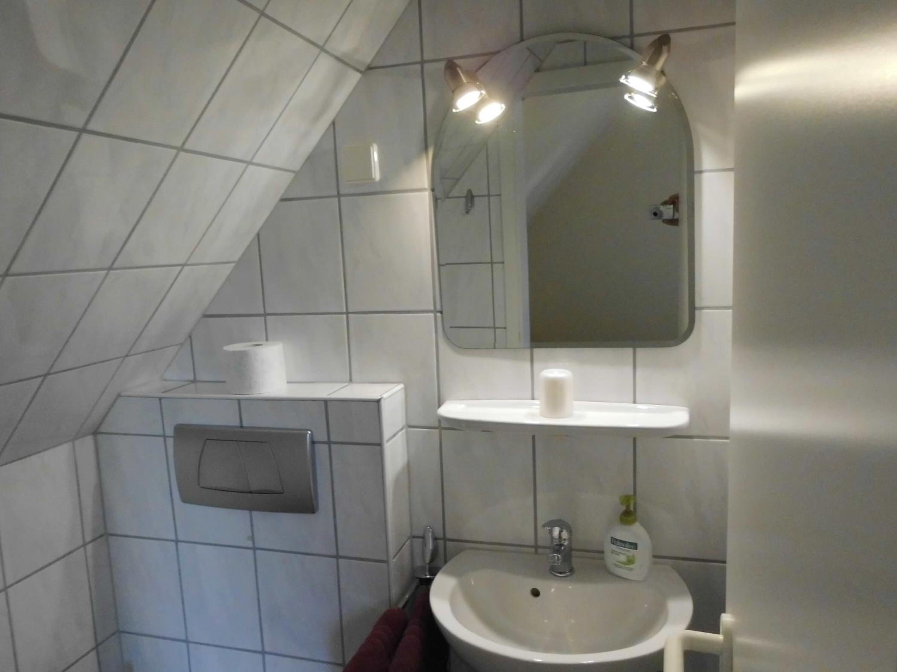 Un baño con un lavamanos blanco, un espejo encima y un perchero para toallas.