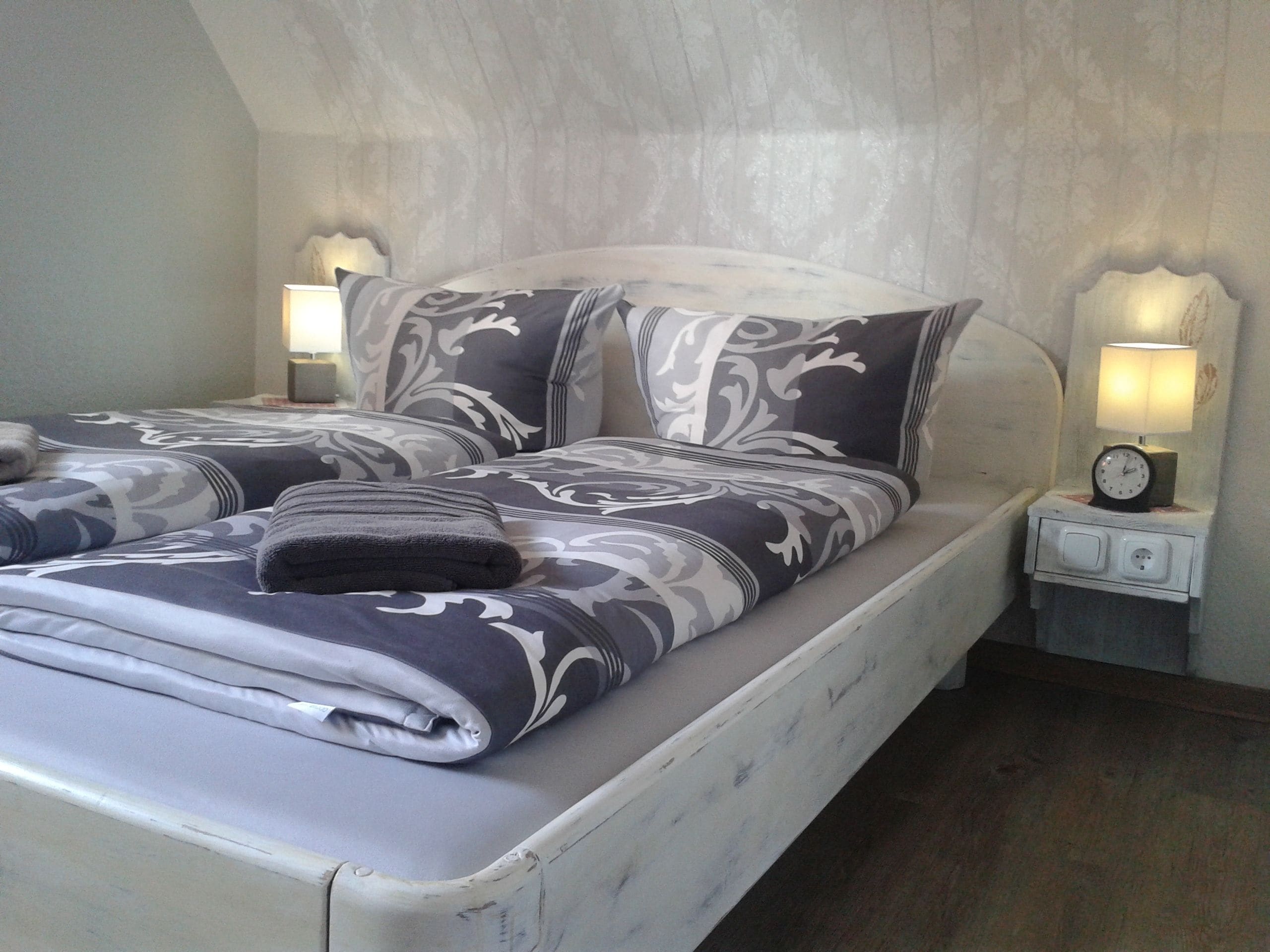 Una cama doble con ropa de cama estampada, dos lámparas de noche y una mesita de noche con un reloj.