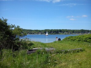 Un lac avec un voilier, des berges verdoyantes et une colline boisée en arrière-plan.