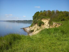 Un paysage naturel comprenant une étendue d’eau, des zones herbeuses et une falaise sablonneuse.