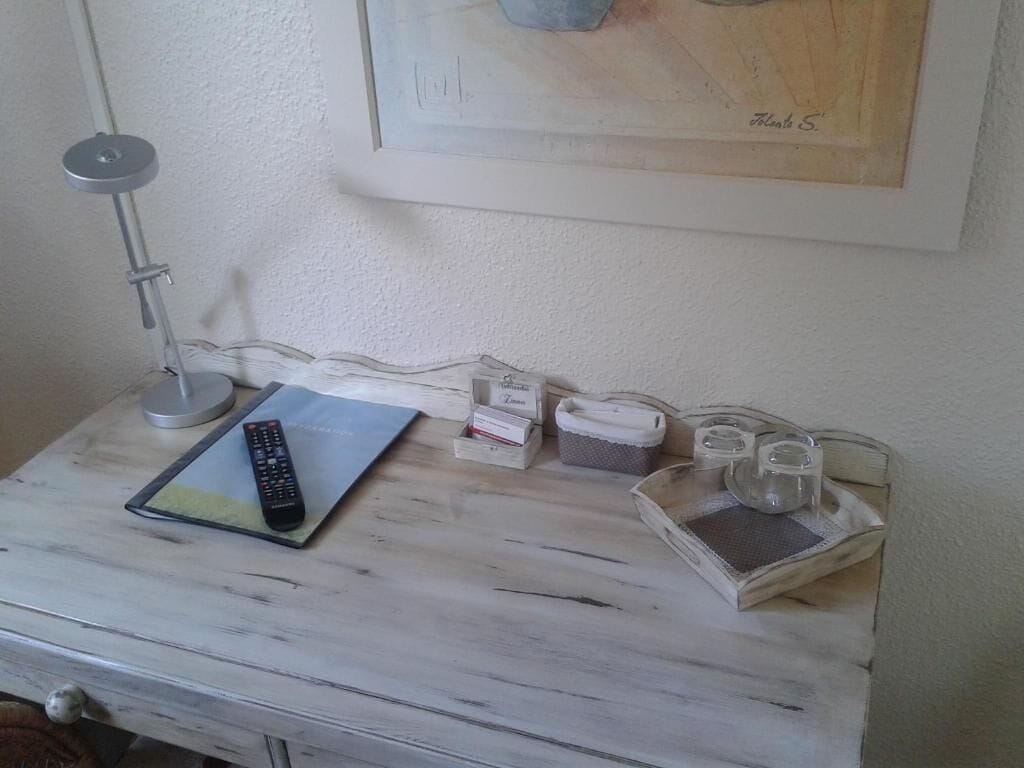 A white wooden table with a remote control, a notebook, and some containers.