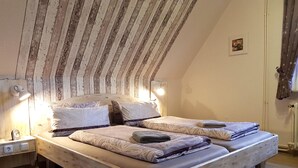 Un dormitorio con techo inclinado, estructura de cama de madera, dos mesitas de noche con lámparas y una pequeña foto en la pared.