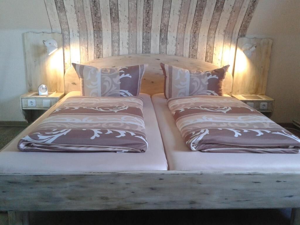 Una cama doble con cabecera de madera, dos mesitas de noche con lámparas y ropa de cama estampada.
