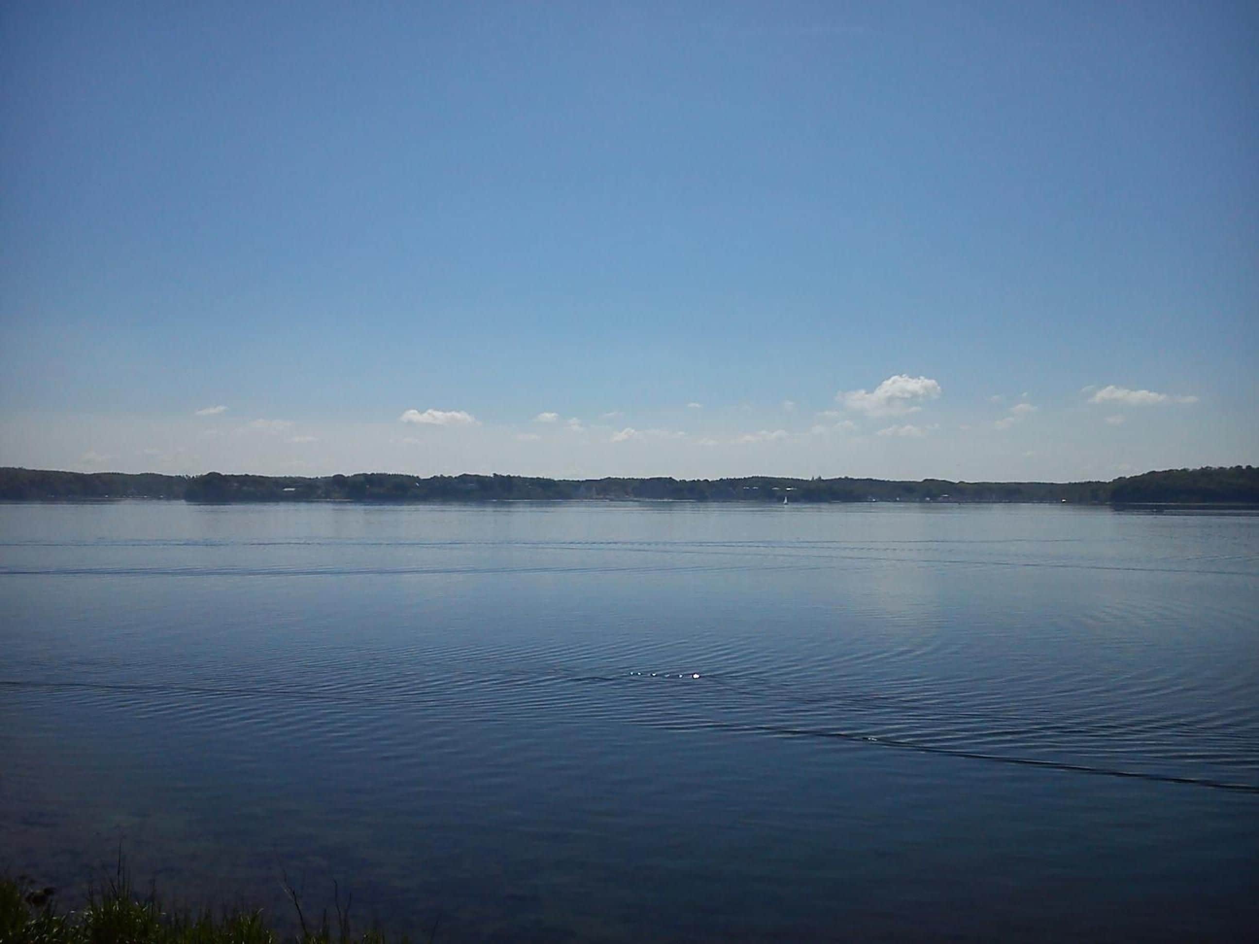 A calm lake with a clear sky and distant land.