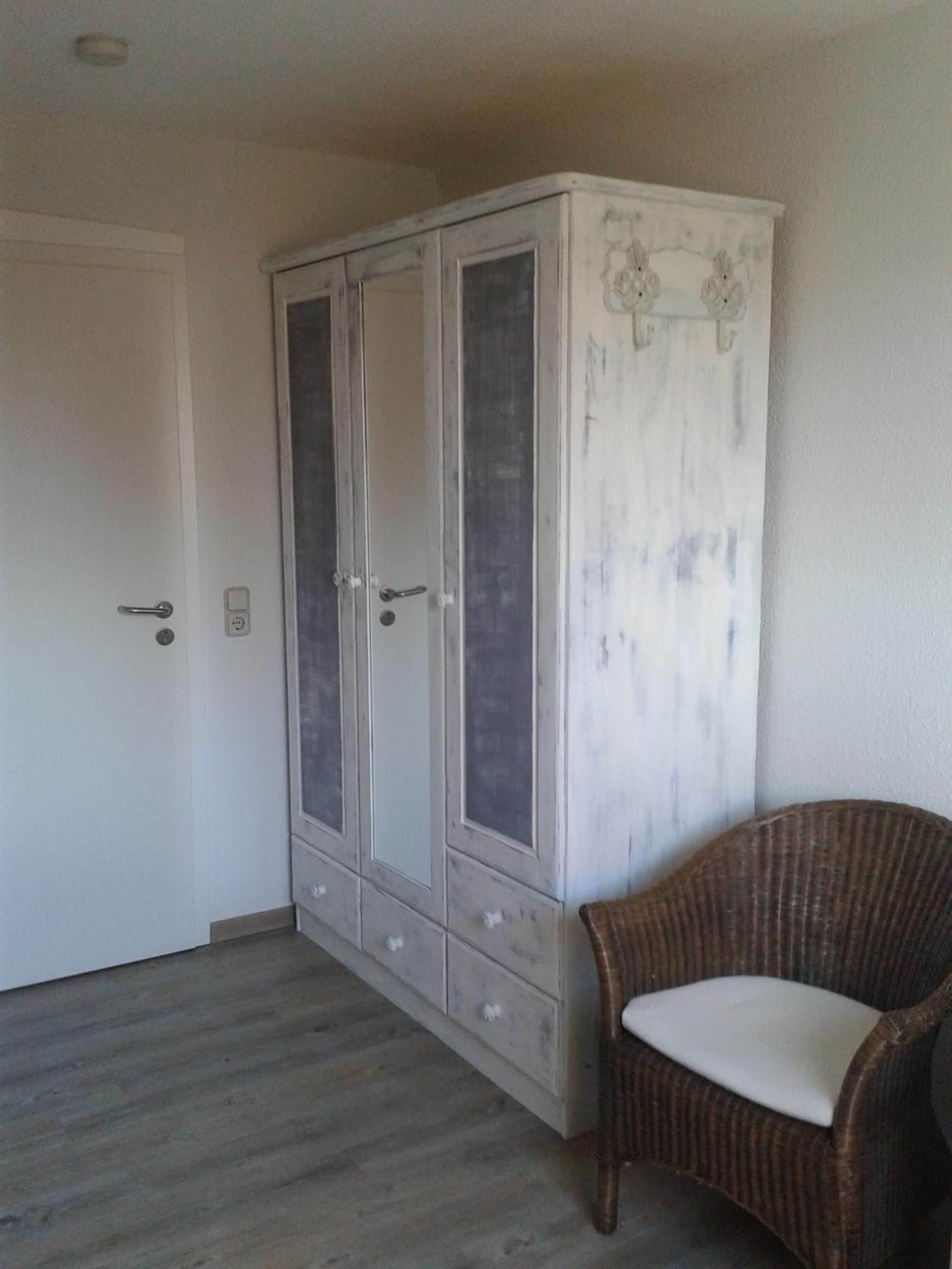 Une pièce avec une armoire blanche, une chaise en osier et un plancher en bois.