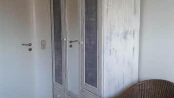 Une pièce avec une armoire blanche, une chaise en osier et un plancher en bois.