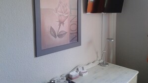 Una obra de arte enmarco con una rosa en la pared, un televisor de pantalla plana montado encima y una mesita de noche con una lámpara y algunos objetos.