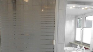 Un baño con ducha de vidrio, lavamanos blanco y espejo sobre él.