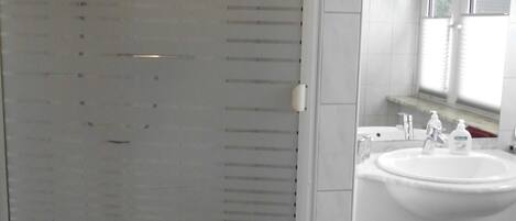 A bathroom with a glass-enclosed shower, a white sink, and a mirror above it.