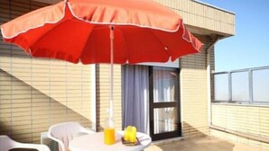 A balcony with a red umbrella, white plastic chairs, and a small table with a drink. - Hotel Palanca (Porto)