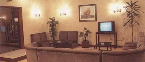 A living room with a sofa set, a television on a stand, a potted plant, and a framed picture on the wall.