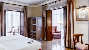 Una habitación de hotel con una cama grande, un armario de madera, un escritorio con una silla y una mesa de comedor.