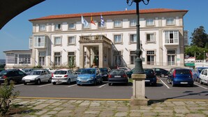 Un edificio grande con varias banderas, un estacionamiento con distintos autos y una farola.