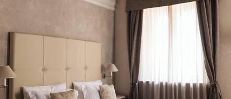 A hotel room with a large bed, two bedside tables, a wall-mounted lamp, and a window with curtains.