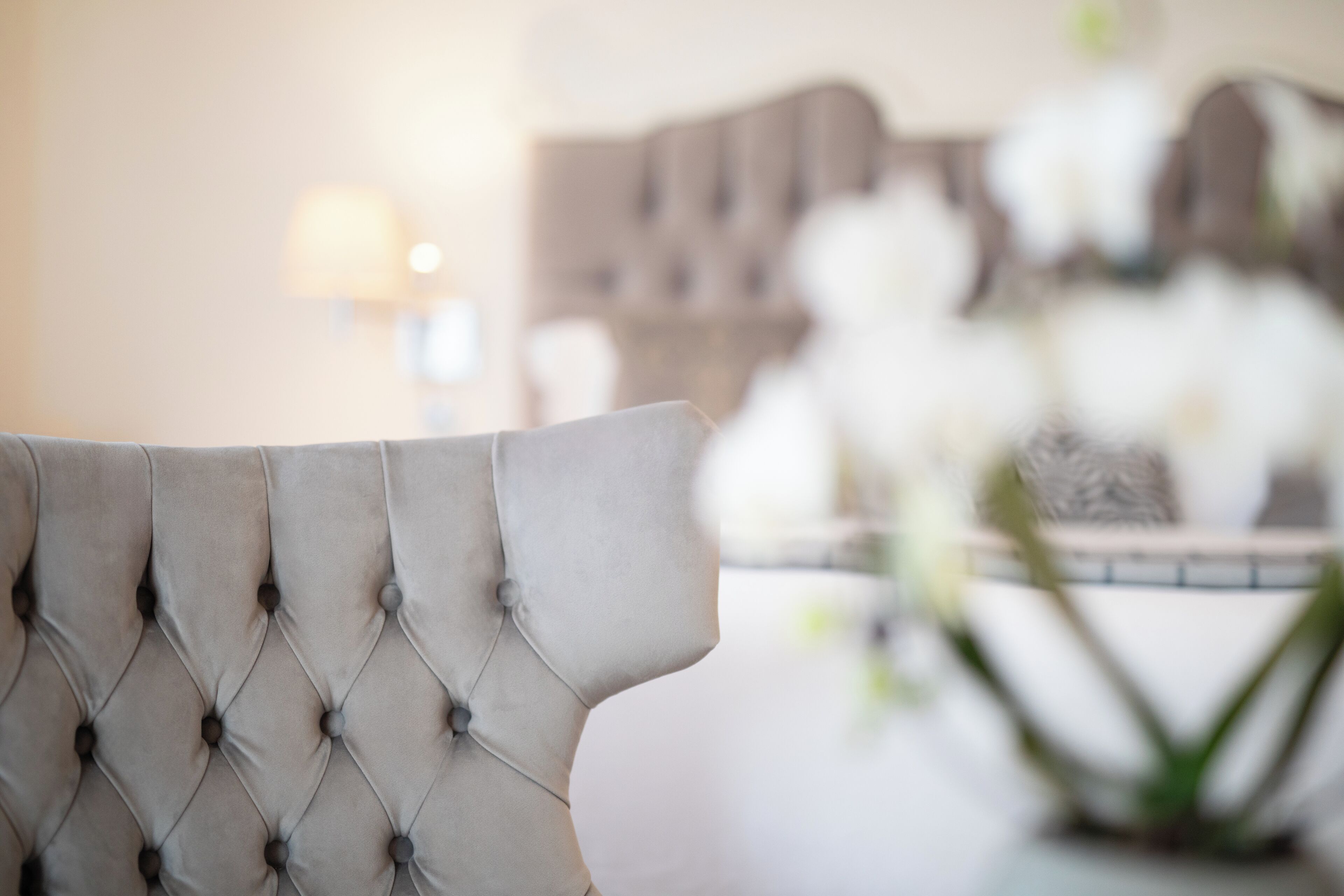 Un fauteuil à dossier capitonné et un vase rempli de fleurs blanches.