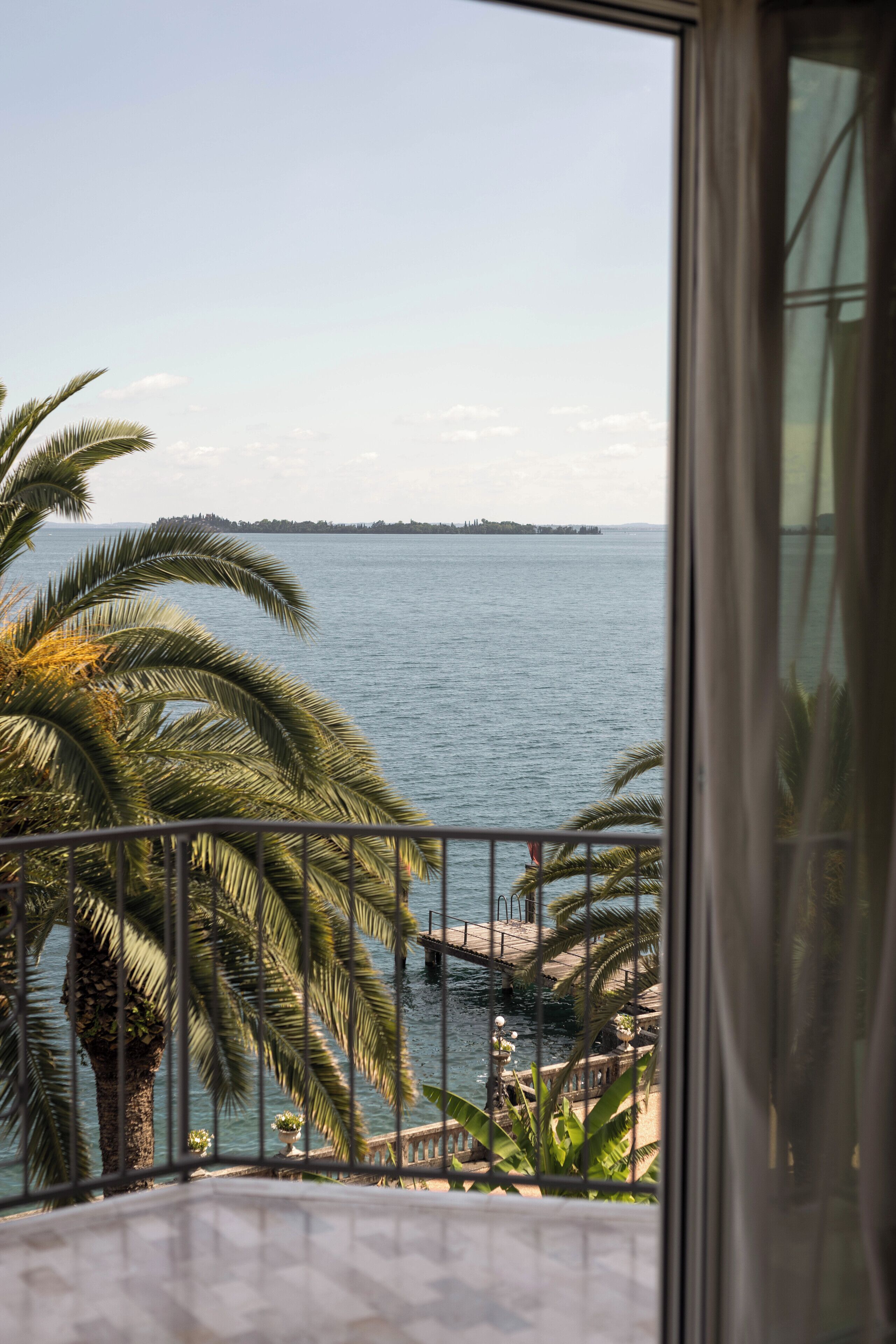 Un balcón con vista al mar, palmeras y una costa lejana.