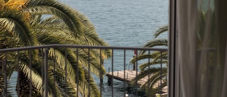 Un balcón con vista al mar, palmeras y una costa lejana.
