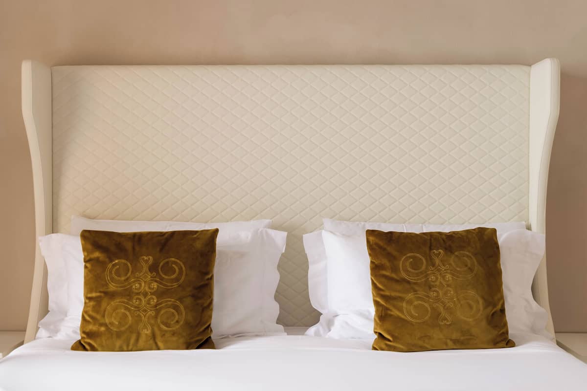 Un lit avec une tête de lit matelassée, deux oreillers blancs et deux oreillers marron ornés d’un motif décoratif.