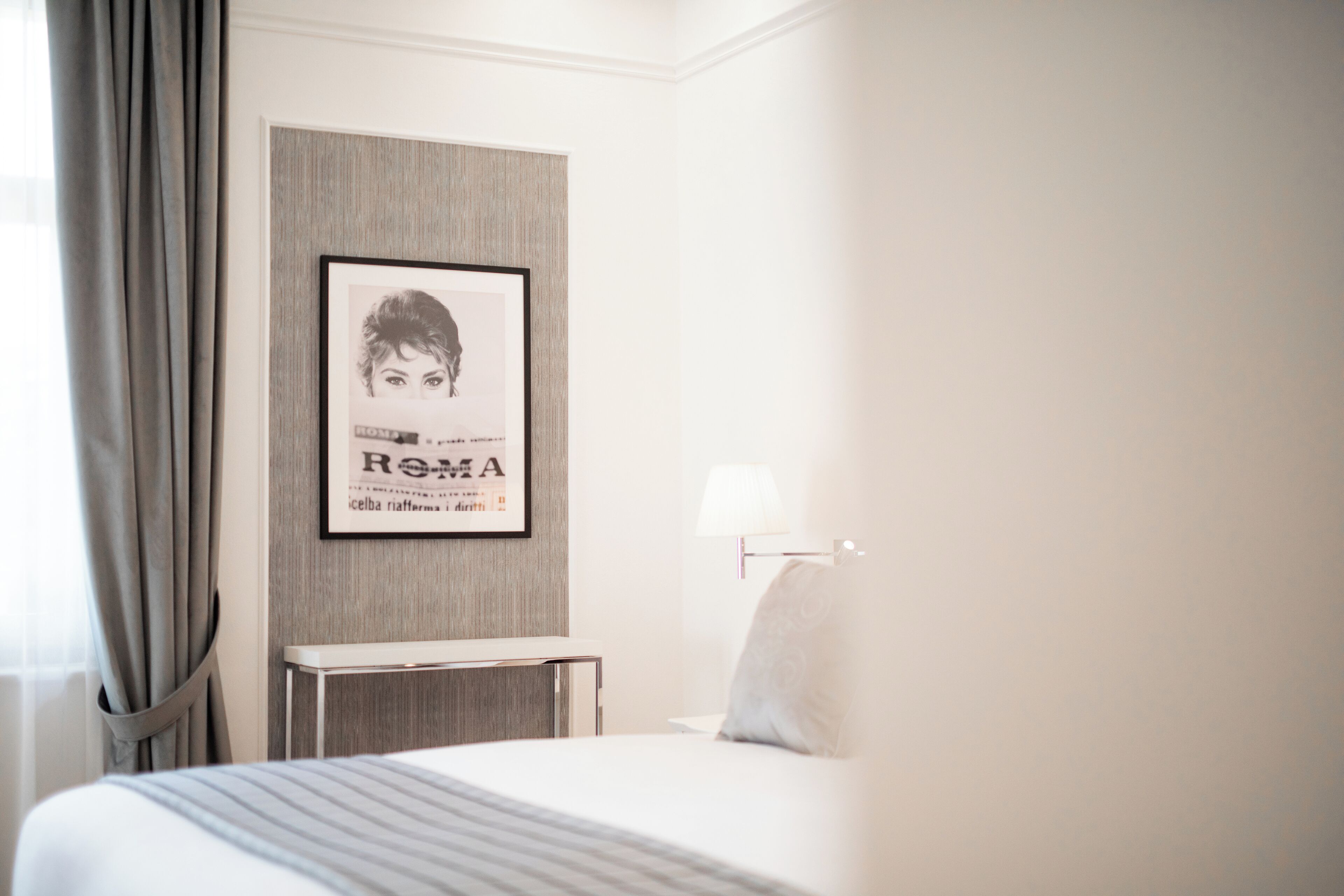 A hotel room with a bed, a bedside table, a lamp, and a framed picture on the wall.