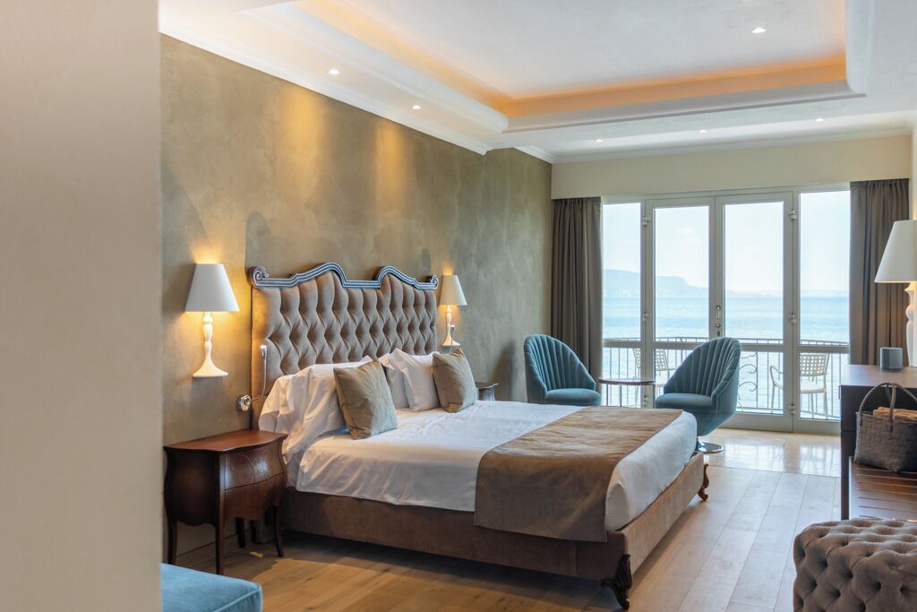 Une chambre spacieuse avec un grand lit, une vue sur la mer et un balcon équipé de chaises.