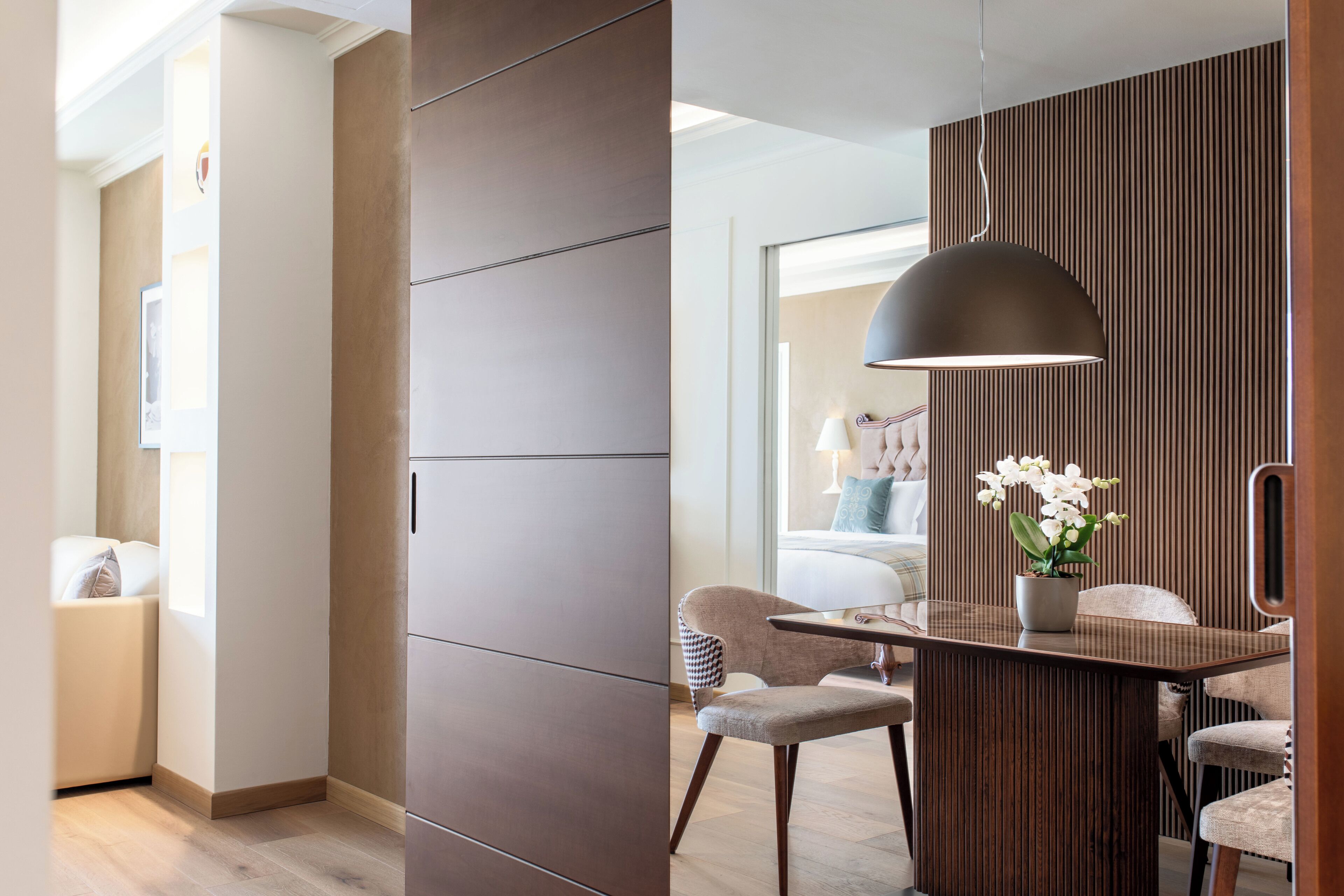 A modern hotel room with a wooden partition, a dining area with a table and chairs, and a hanging pendant light.
