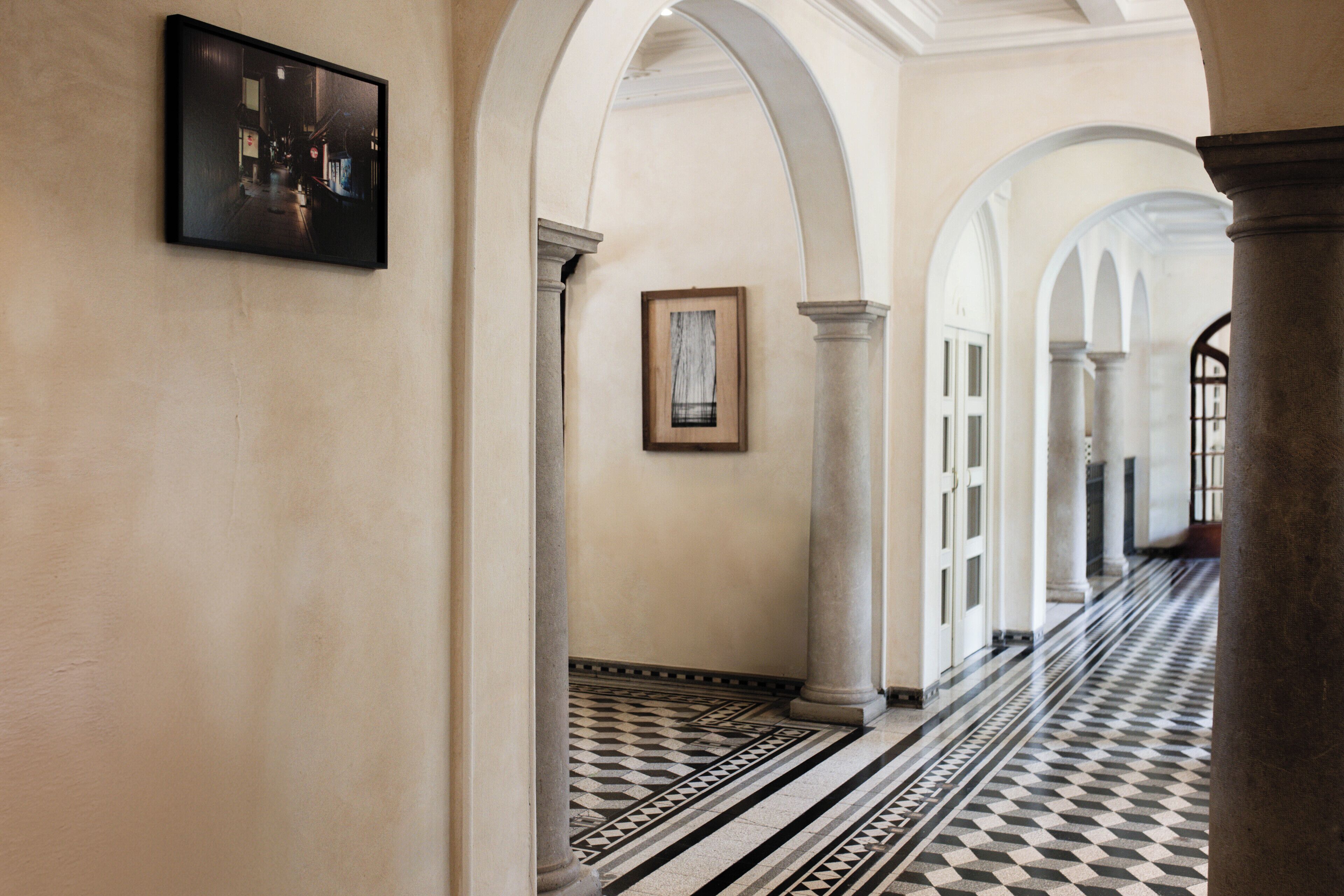A corridor with white columns, a patterned floor, and framed artwork on the walls.