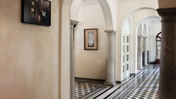 Um corredor com colunas brancas, piso estampado e obras de arte emolduradas nas paredes.
