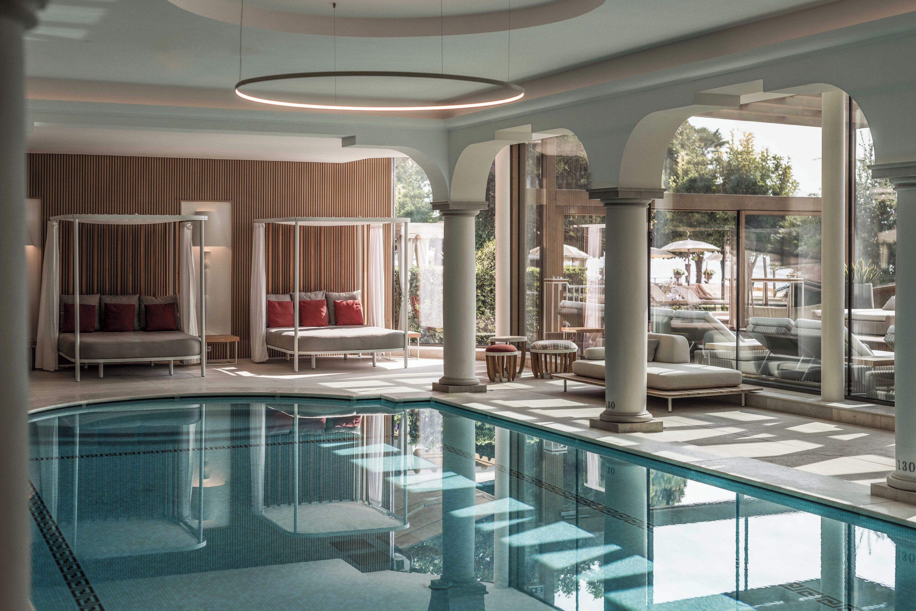 A luxurious indoor pool area with a seating area, columns, and a view of the outdoors.