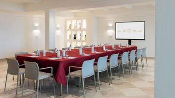 Un salón de conferencias con una larga mesa, sillas, una pantalla de proyector y estanterías con objetos decorativos.