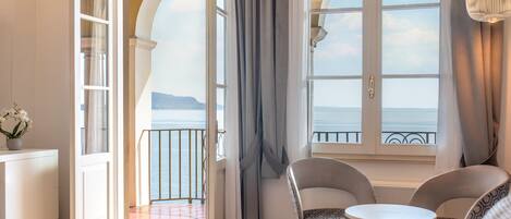 A hotel room with a bed, a small table, two chairs, a view of the sea, and a balcony with a railing.