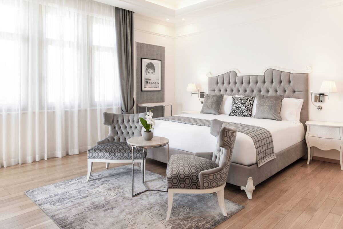 Une chambre à coucher moderne avec un grand lit, deux fauteuils, une petite table et un vase décoratif.